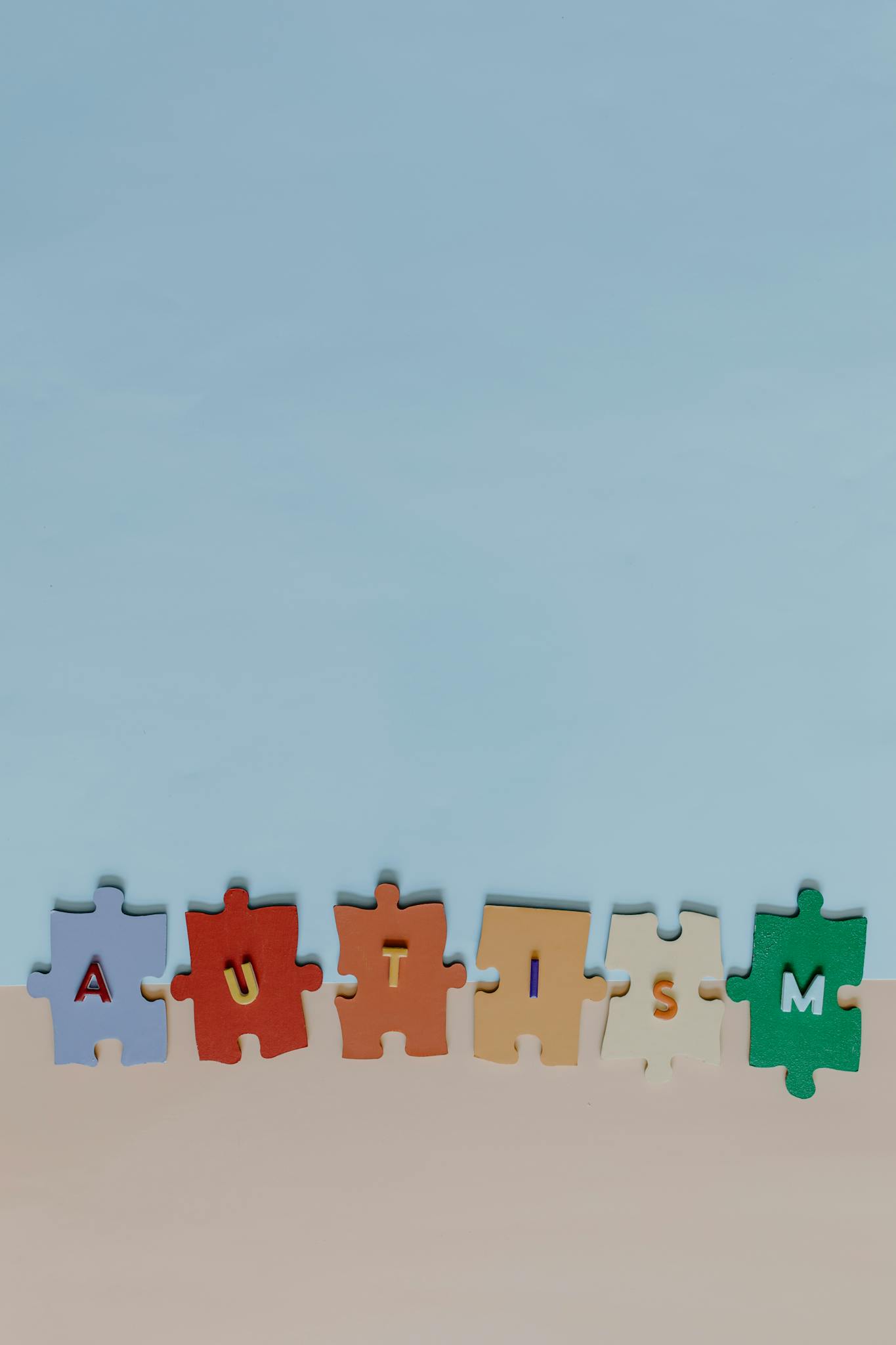 Vertical shot of autism awareness puzzle pieces spelling 'AUTISM' on a pastel background.