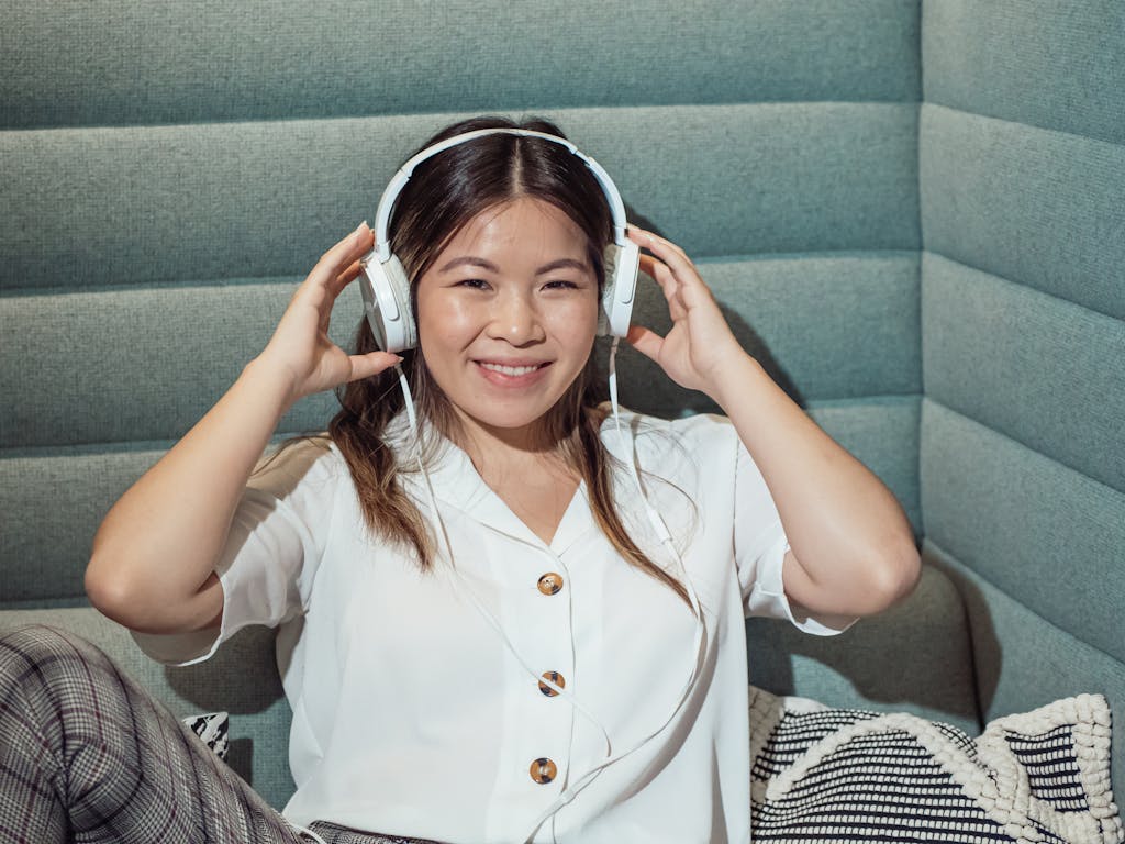 Young woman with headphones sitting indoors, smiling while listening to music.