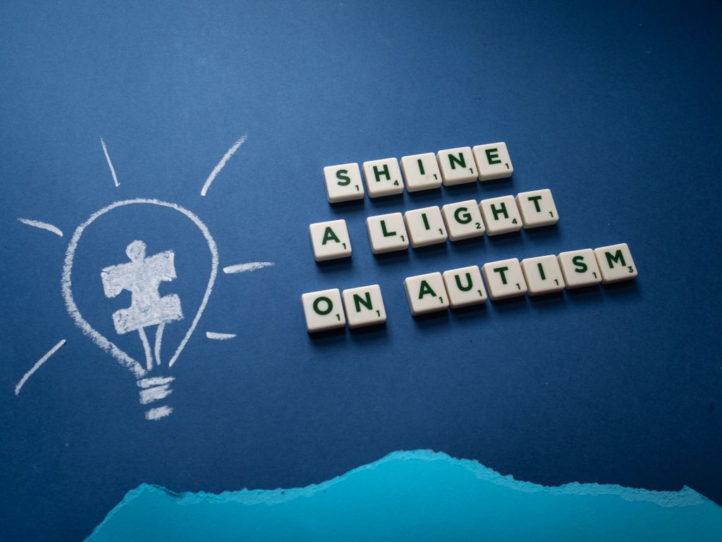 Creative representation of autism awareness with puzzle piece lightbulb and Scrabble tiles message on blue background.